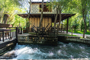 Powerful energy of flowing river turns traditional wooden water wheel at ancient Konigil Meros paper factory in Samarkand. Strong stream creates foam and motion in sunny day. © diy13