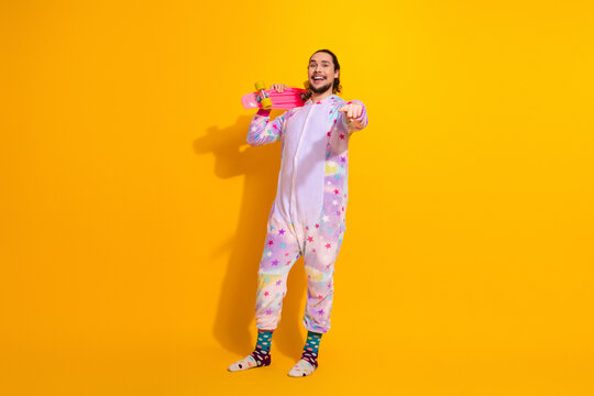 Playful man in pastel unicorn pajama with skateboard against bright yellow background fashion lifestyle