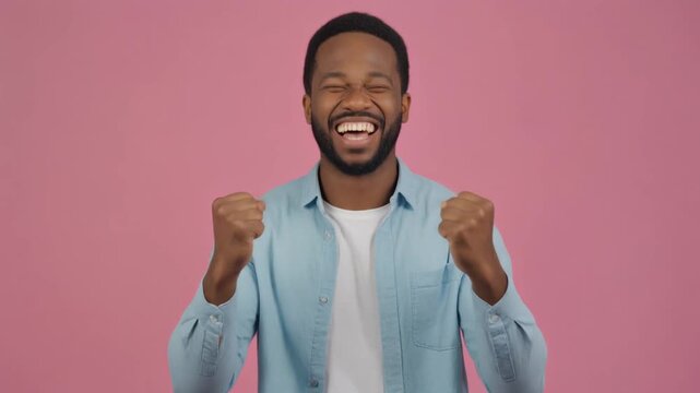 Joyful African American Man Celebrating Success with Fists Pumped Isolated on Pink Background
