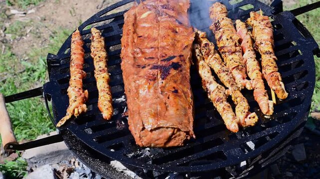 A rack of marinated pork ribs and several small meat skewers continue to cook on a round charcoal grill, with the ribs showing prominent grill marks
