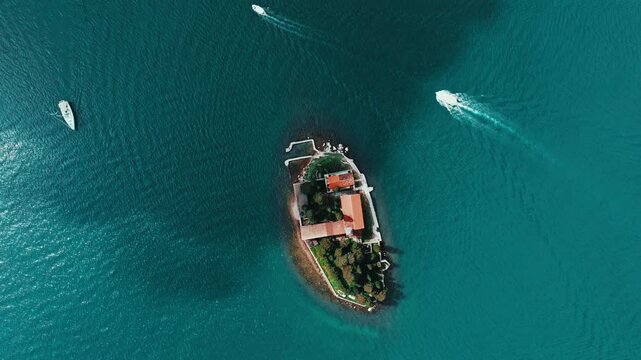 Cinematic aerial drone footage of Our Lady of the Rocks near Perast. Historic island church surrounded by the turquoise waters of the Bay of Kotor with dramatic mountain scenery