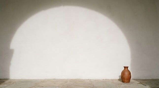 Small terracotta clay vase standing on a stone floor against a textured wall with a large soft circular light shadow