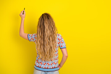 Woman writing on a bright yellow wall with a pen, seen from the back with long wavy hair wearing a patterned sweater in a casual creative pose © deagreez