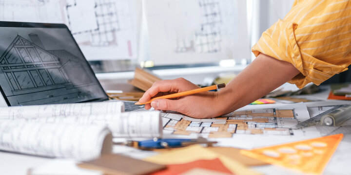 Interior design process with hands selecting wood sample over architectural plans, floor plan, laptop and color palette, residential renovation planning and material selection concept.