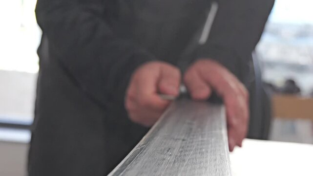 Handheld close up video shows hands manually sharpening ski edge with metal tool while ski is fixed in workshop vise during detailed winter sports maintenance 2026