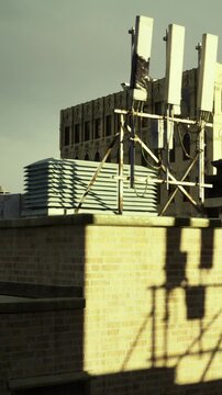 A scene shows a rooftop with stacked construction materials and a view of an old building. The sun casts shadows on the bricks. This is a common sight in urban areas.