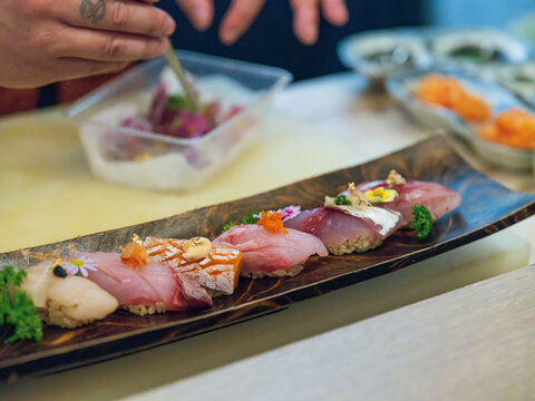 Chef Plating Nigiri with Edible Flowers on Long Wooden Omakase Tray