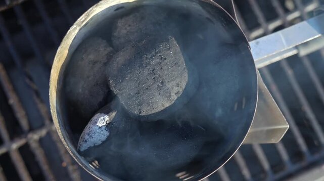 Top view of charcoal briquettes smoking in chimney starter on grill grate
