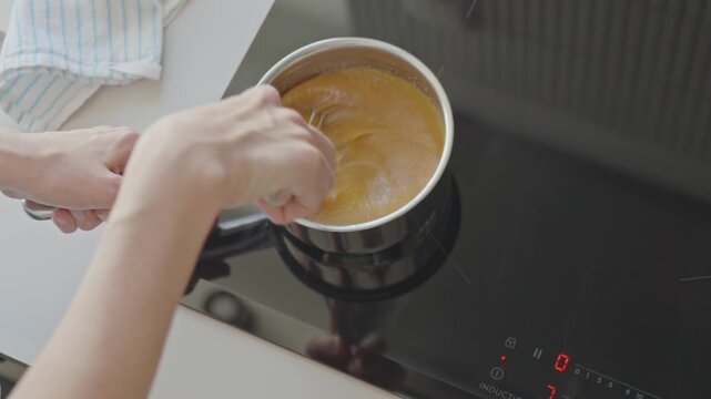 Woman stirs mixture with whisk in stainless saucepan on induction cooktop