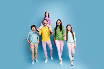 Naklejka premium Happy family portrait of parents and three children walking together in colorful casual clothes against a blue studio background