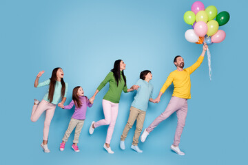 Naklejka premium Family holding colorful balloons and playfully jumping together against a blue background, parents and children enjoying a joyful, carefree moment