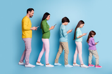 Fototapeta premium Family walking in a row looking at smartphones — parents and children using mobile phones against a blue background