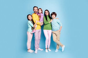 Fototapeta premium Smiling family portrait of parents with three children standing together against a blue background, casual clothing, warm togetherness and happy family moment