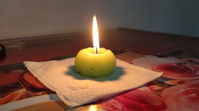 Burning pumpkin shaped candle on wooden table in dark cozy room