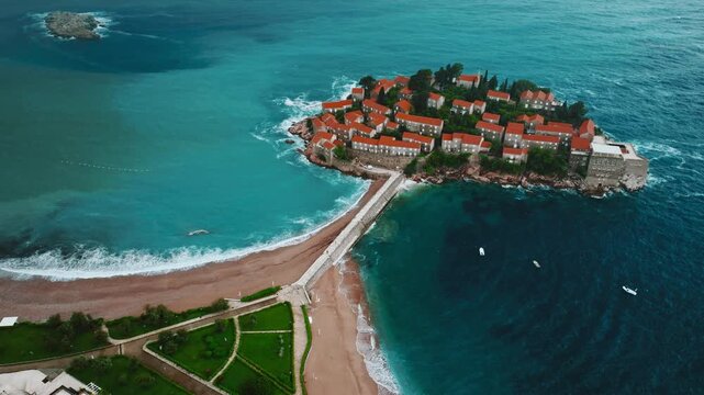 Cinematic aerial drone footage of Sveti Stefan featuring the iconic island village connected to the mainland by a narrow causeway, surrounded by turquoise Adriatic waters