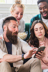 Fototapeta premium Diverse friends sharing smartphone screen laughing at home
