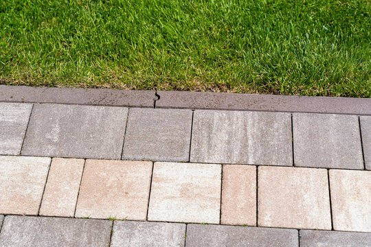 Close-up view of textured concrete pavers contrasting with lush green grass, illustrating landscaping design and outdoor aesthetics in a residential setting