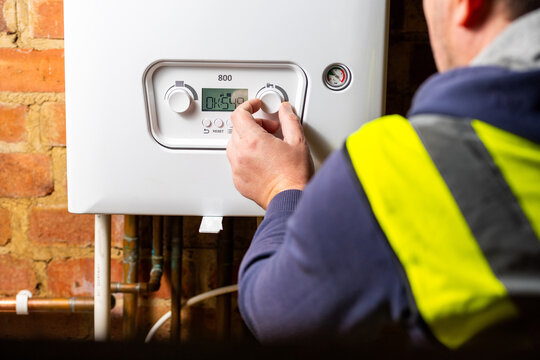 Men hand setting temperature button on control panel of central heating at combi boiler. Incressing price for gas