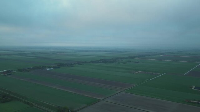 Aerial view of vast green polders and agricultural fields under a misty overcast sky in Schermerhorn, North Holland, Netherlands.