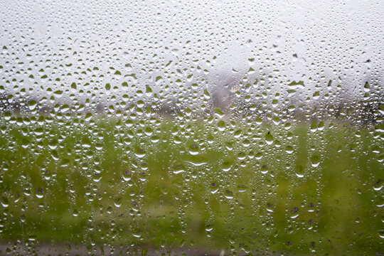 Raindrops on window glass with soft blurred background, moody atmosphere and shallow depth of field, ideal for weather, melancholy, autumn and rainy day concepts.