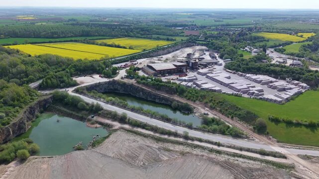 Aerial view of Marshalls industrial site featuring a quarry pond and stacks of materials surrounded by green and yellow fields in Maltby, England, United Kingdom.