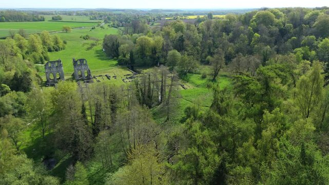 Aerial view of the historic Roche Abbey ruins nestled within dense green woodland and rolling hills under a bright sky in Maltby, England, United Kingdom.