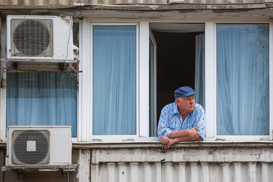 Senior man coping with urban heatwave in apartment window