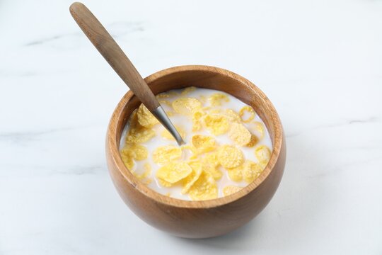 Bowl of delicious cereal with milk and spoon on white marble table, closeup