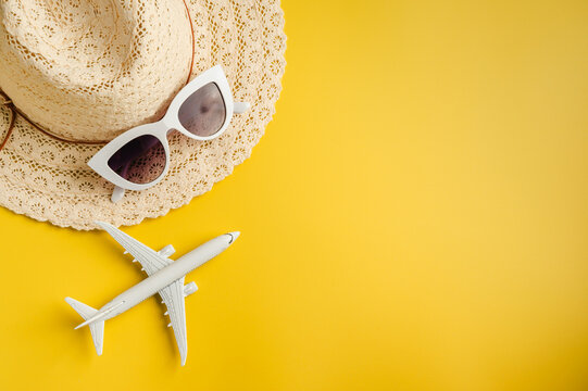 Travel-themed flat lay, summer holiday background. Toy model airplane, sunglasses, sun hat over yellow backgrounds, copy space