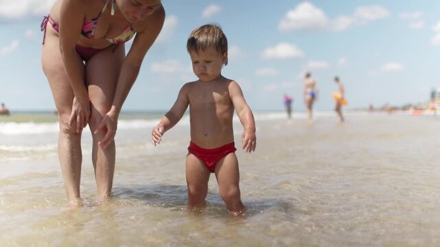 The kid collects shells and pebbles in the sea on a sandy bottom with his mother under the summer sun on vacation
