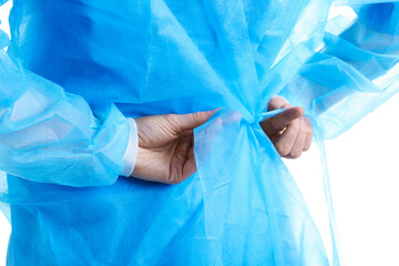 Fototapeta premium Medical worker tying disposable isolation gown on white background, closeup