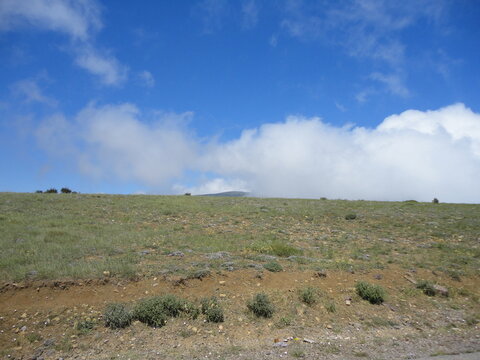 Scenic view of dramatic clouds contrasting with the blue sky over a green mountain meadow near Tarom, Iran. This vibrant summer landscape captures the high-altitude natural beauty.