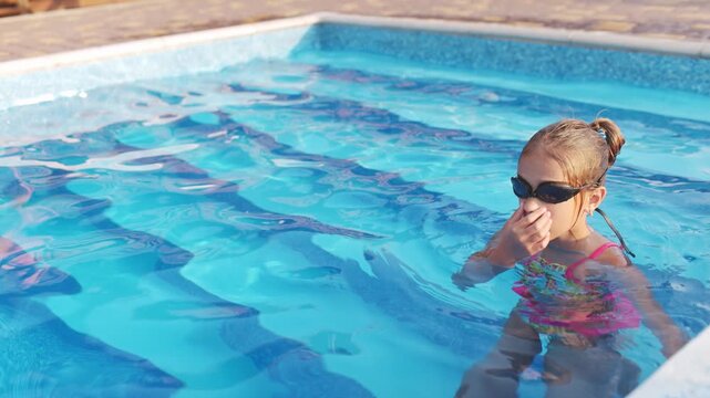 A girl in a bright swimsuit with swimming goggles dives into a pool with clear transparent water