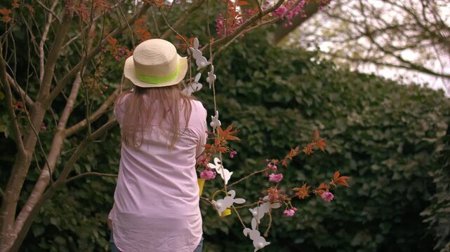 Woman wearing Easter bonnet and sits by easter decorations on blossom tree