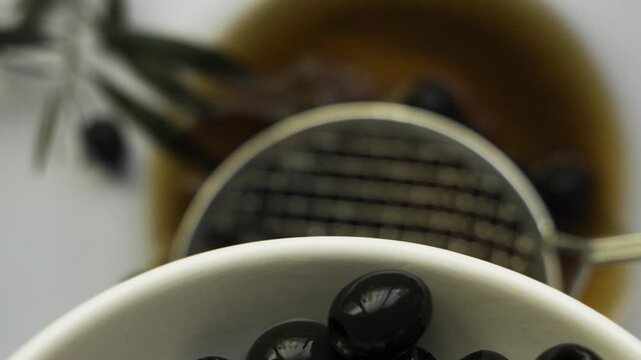 Black_pitted_olives_accumulating_in_white_bowl_with_skimmer_motion_on_white_surface_4k_120fps