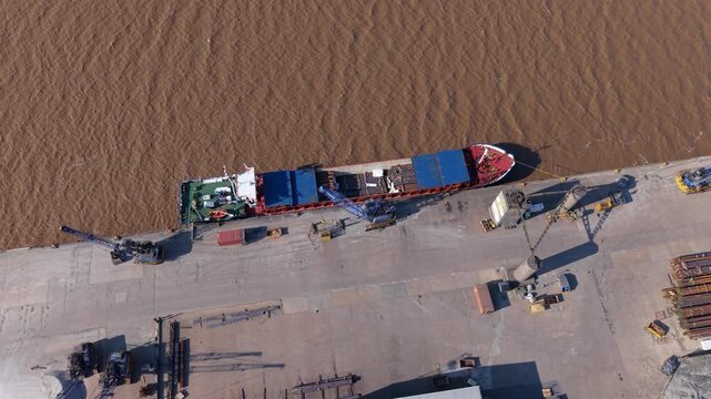 Aerial view of a cargo ship docked at PD Ports with industrial cranes and containers along the river bank in Scunthorpe, England, United Kingdom.