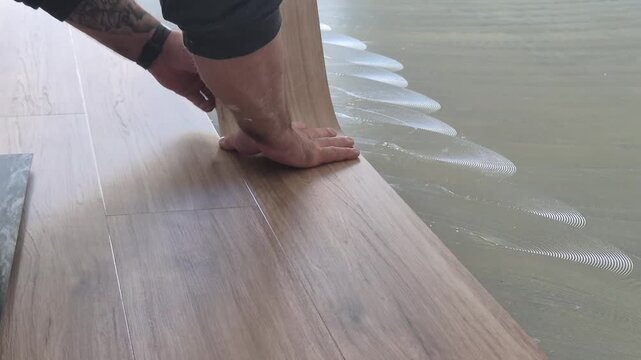 Close up of a professional flooring installer placing a self-adhesive vinyl plank onto the floor.