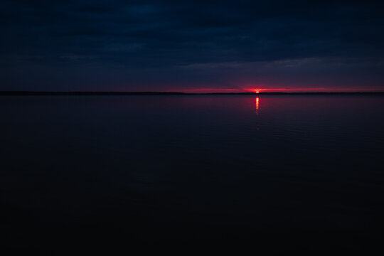 Sunset on the lake. Evening sky with beautiful solar disk is reflected in the water of the lake