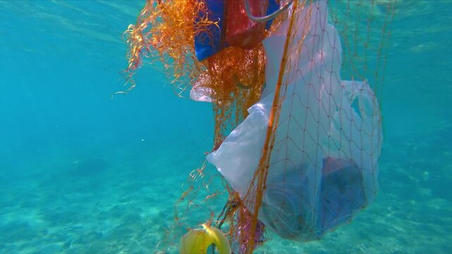 Close-up shot of entangled plastic debris in clear blue water. The scene shows pollution, including bags and fishing nets, highlighting environmental damage in marine settings.