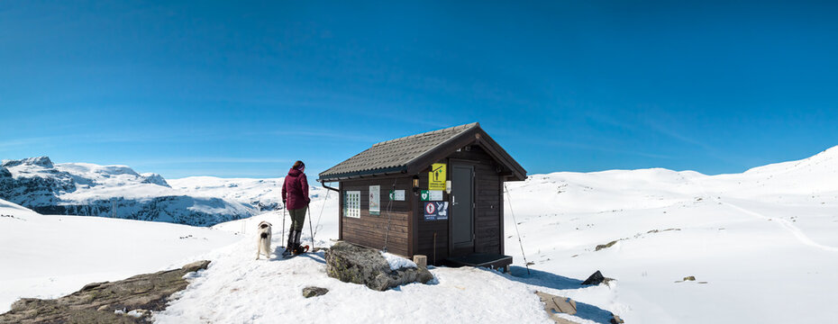 Person und Hund an H&uuml;tte in winterlicher Hochlandschaft