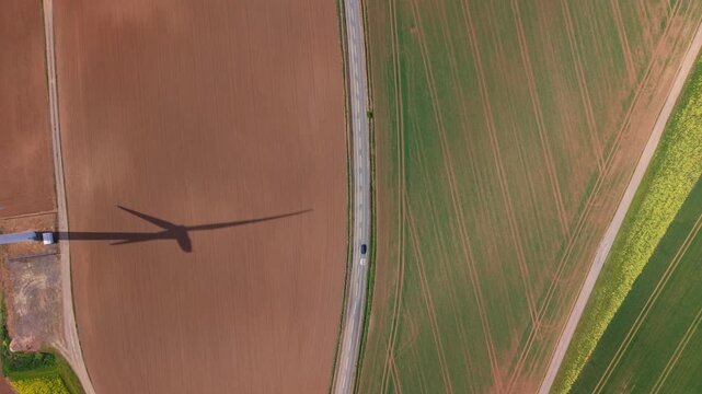Aerial view of Marr Wind Farm turbine shadow cast across a brown field next to a rural road and green farmland in Marr, England, United Kingdom.
