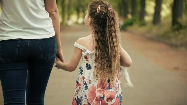 Mother Holding Hands with Daughter While Walking in Park. Happy Family Enjoying Leisure Time Together. Weekend Relaxation in Garden