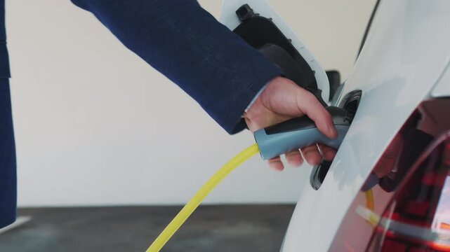 A person is seen plugging a blue EV charger into a white electric vehicle, highlighting the ease of use at a modern charging station.
