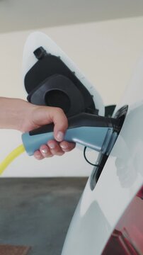 A person is charging their electric car, connecting the plug to the port. The scene takes place in a modern garage, highlighting the convenience of home charging for electric vehicles.