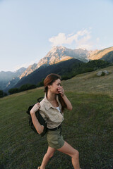 Fototapeta premium Young woman with backpack hikes across a grassy mountainside, enjoying a sunny day and fresh air, in casual utility outfit as mountains loom in the background.