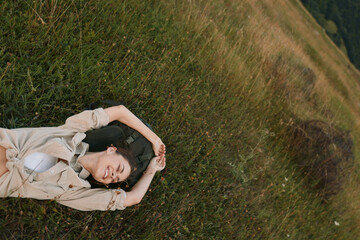 Naklejka premium Young woman rests on grass in a sunlit meadow, eyes closed, wearing a light beige shirt, conveying calm relaxation and connection with nature.
