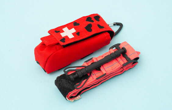 Red medical pouch with a first aid cross and a tactical tourniquet for emergency bleeding control on a blue background.