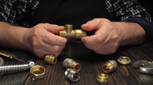 Hands of a male plumber assembling brass plumbing fittings on a wooden workbench with various tools and components visible in the background