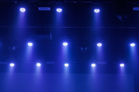 Cool blue LED stage lights shine through haze from a dark ceiling rig, creating a moody concert or theater background with copy space