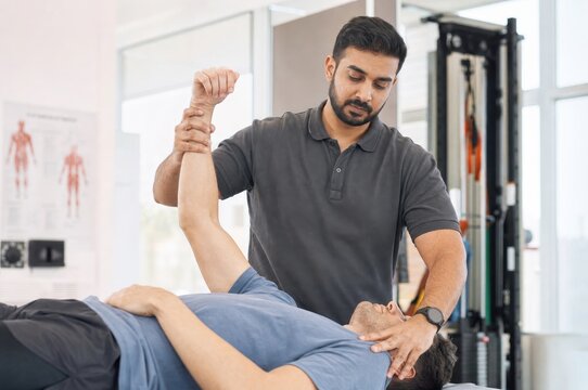 physiotherapist assisting male patient shoulder stretch on treatment table rehabilitation clinic physical therapy